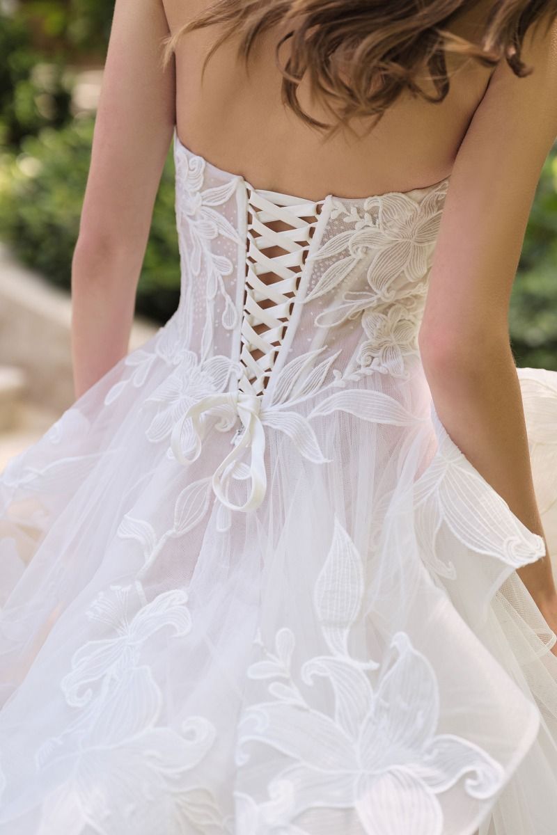 Vestido de novia que presenta un escote corazón sin tirantes y un corpiño semitransparente con varillas y una falda de tul escalonada en cascada está adornada con un delicado diseño floral de lirios estrellados