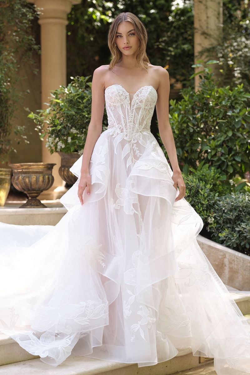 Vestido de novia que presenta un escote corazón sin tirantes y un corpiño semitransparente con varillas y una falda de tul escalonada en cascada está adornada con un delicado diseño floral de lirios estrellados